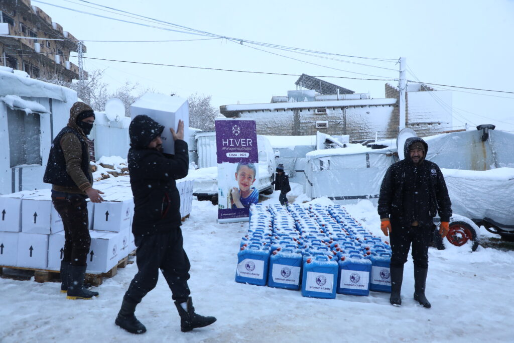 Des personnes se tenant dans une file d'attente, visiblement fatiguées, attendent de récupérer de l'aide alimentaire et des bidons de fioul au Liban en plein hiver, vivant dans des tentes dans des conditions difficiles.