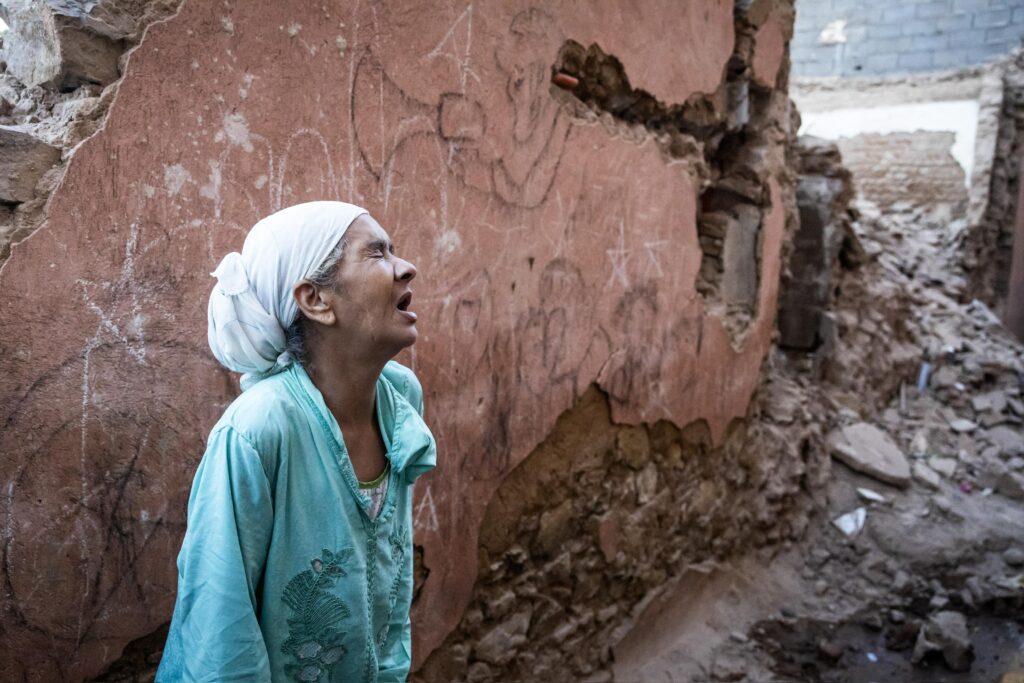 Une femme en détresse, les yeux humides, se tient devant les décombres de sa maison après le séisme au Maroc, exprimant la douleur et la perte causées par cette situation tragique.